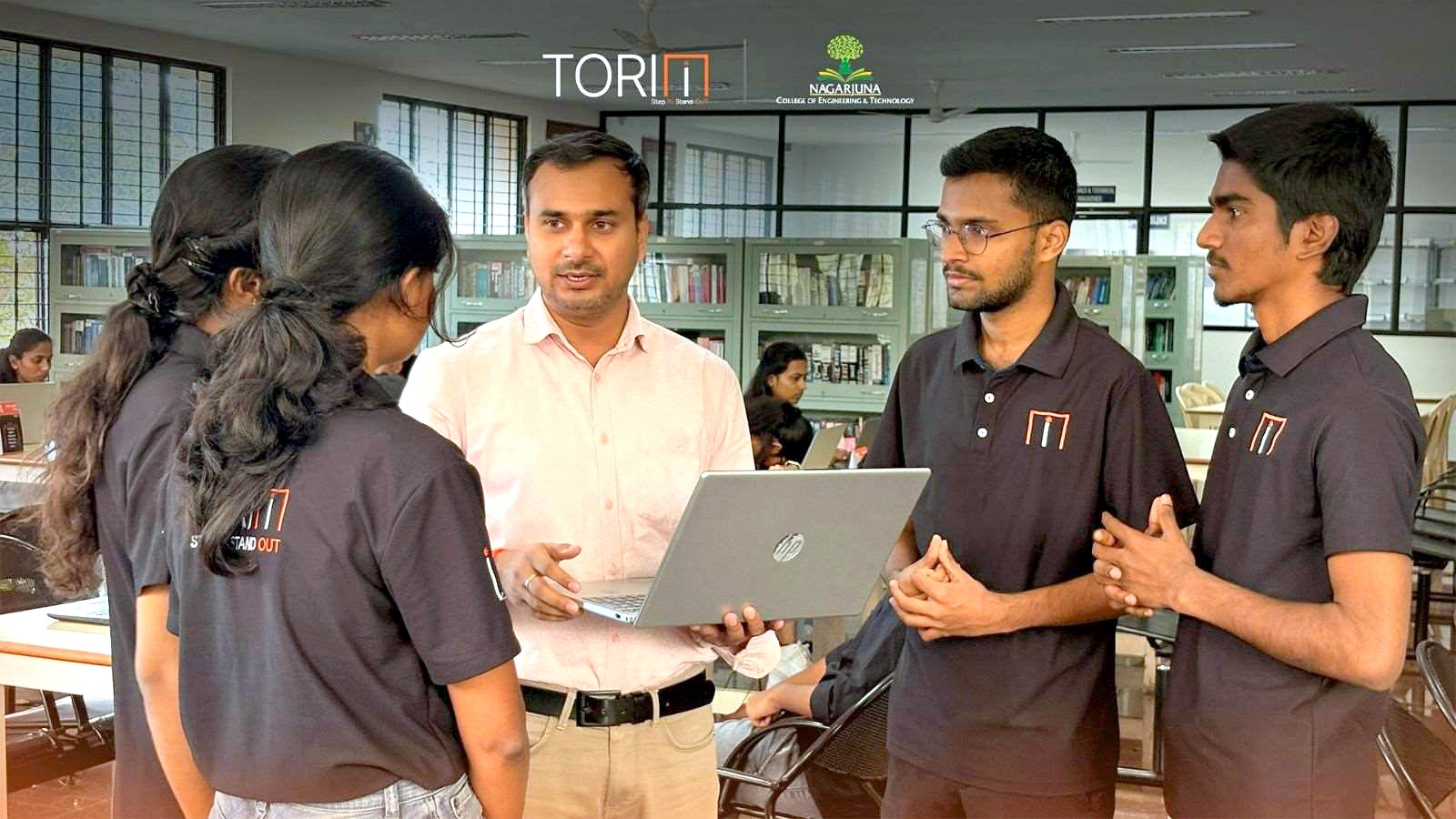 A mentor reviewing a student team's build on a laptop in the library